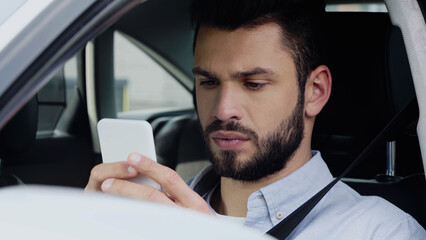 thoughtful man estimating route on smartphone while sitting in car.