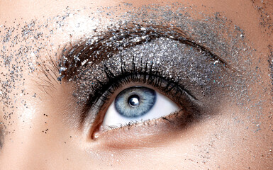 Close Up face detail in studio light. Female natural blue eye with beautiful glitter smokey eyes...