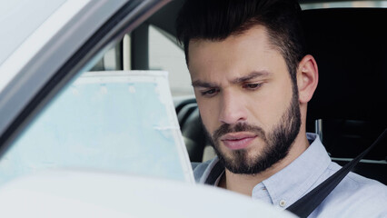 young and thoughtful man estimating location while sitting in car and looking at map.