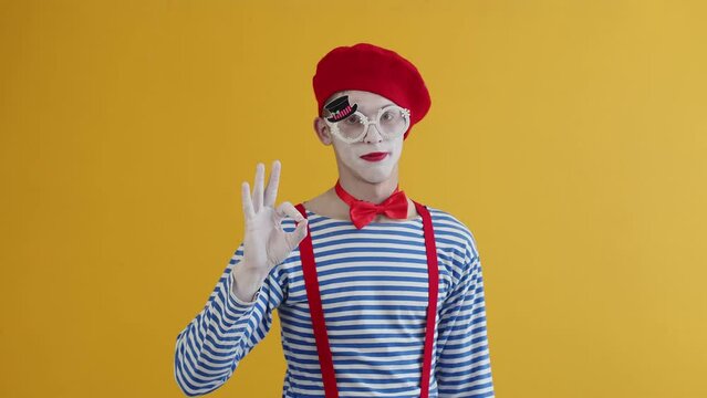 Portrait of a mime clown in glasses, striped shirt, red beret and bowtie making wow expression, doing ok sign with his hand while nodding his head. Approval, admiration, praise, respect concept