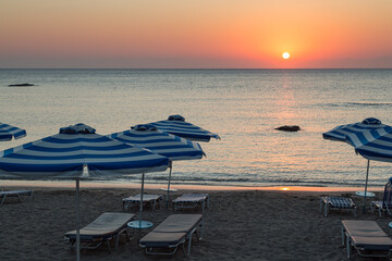 Parasol and sun loungers at sunrise by ocean