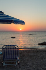 Parasol and sun lounger at sunrise by ocean