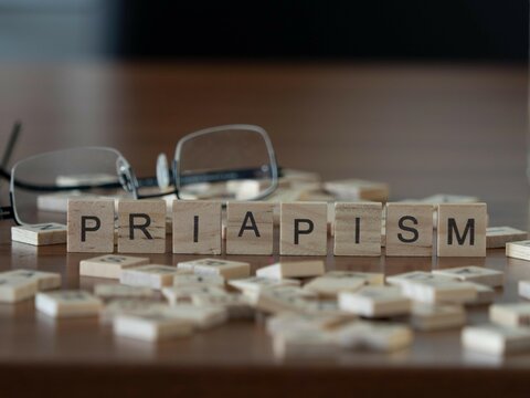 priapism word or concept represented by wooden letter tiles on a wooden table with glasses and a book