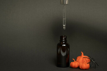 a black serum bottle on a black background with plasticine pumpkins and a spider , a creative...