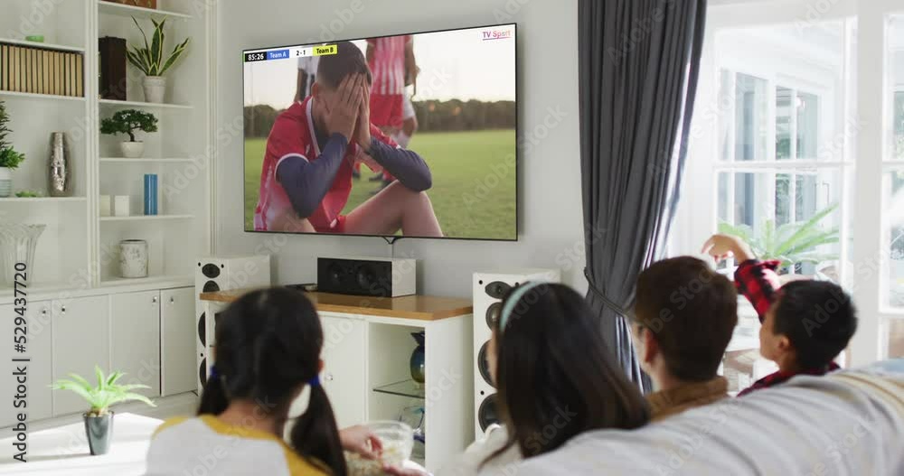 Wall mural Video of asian couple with son and daughter sitting on sofa and watching football at home