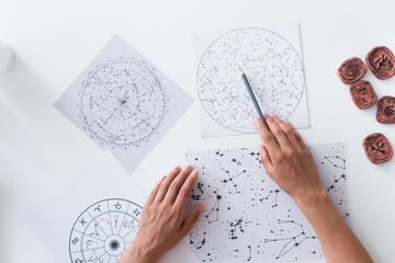 top view of cropped astrologer pointing at celestial map near clay runes.