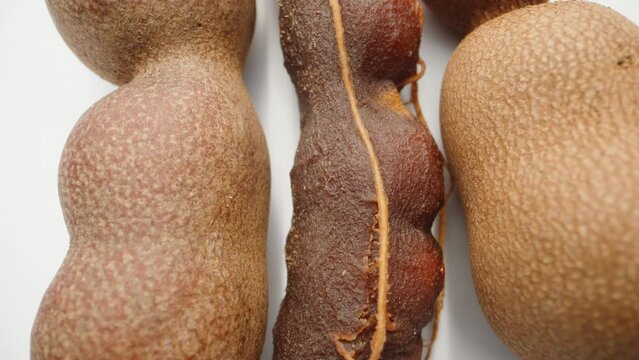 a peeled tamarind fruit between two unpeeled ones. on a white background. Dolly slider extreme close-up.