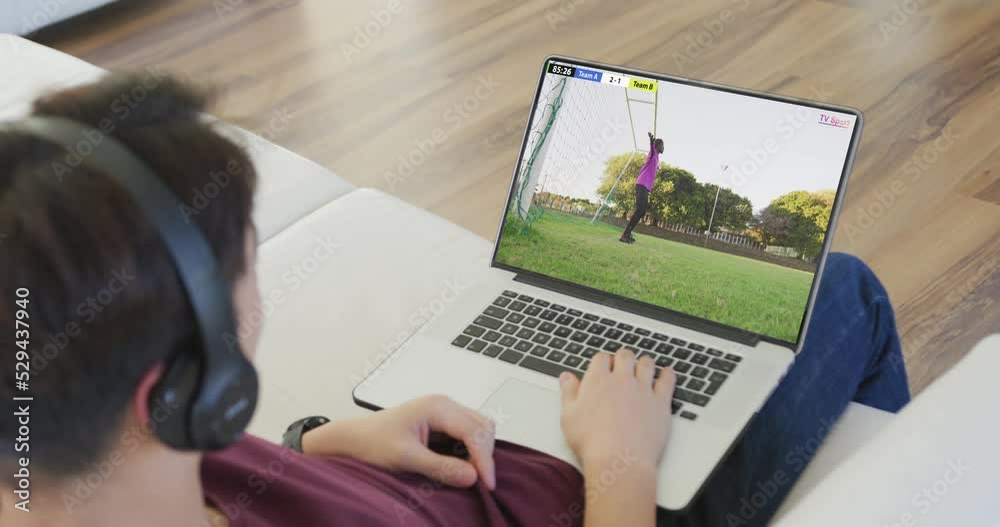 Poster Video of caucasian man sitting on sofa and watching football on laptop at home