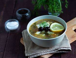 Soup with vegetables, olives and sour cream in a bowl. Spices and salt in a transparent bowl.