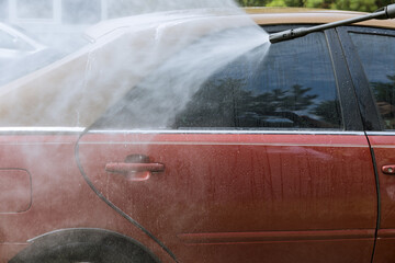 During the process washing his car worker sprays high-pressure jets of water onto his car while simultaneously cleaning it