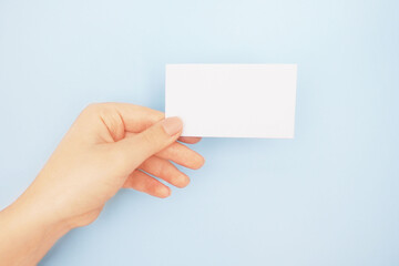   Female hands holding white blank paper sheet mockup on light blue background.