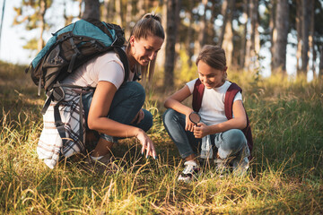 Mother and daughter  explore with magnifying glass nature while hiking.