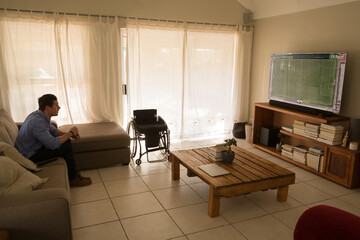 Man with a disability watching football match and sitting on the couch