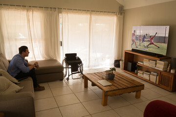 Man with a disability watching football match siting on the couch