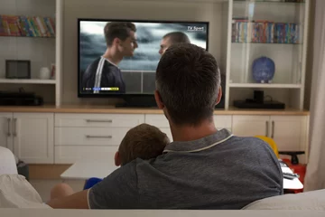 Fotobehang Father and son watching football match siting together on the couch © vectorfusionart