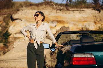Woman road tripping, standing by her car cabriolet