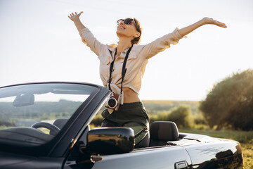 Woman standing in car cabriolet with camera on her neck
