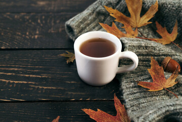 Hot tea and autumn leaves on vintage wood background with sweater - seasonal cozy relax concept. Copy space