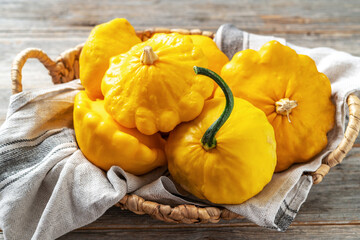 Yellow patisson in a basket on a light gray wooden kitchen table close-up. Autumn harvest of bush...