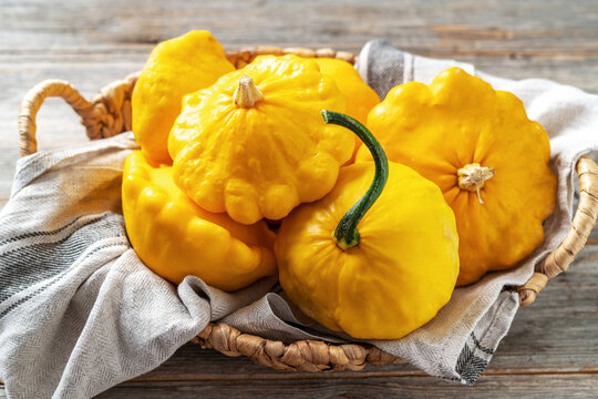 Yellow patisson in a basket on a light gray wooden kitchen table close-up. Autumn harvest of bush pumpkin on a culinary background