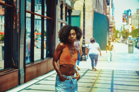 woman with afro hair and urban clothing standing outside on sidewalk