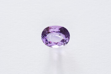 Genuine violet amethyst gemstone. Natural mined and faceted in Brazil. Unheated gem setting for jewelry making. Oval shaped clean and transparent purple color stone. White background daylight window.