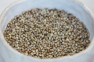 Dried hemp cannabis seeds in a white ceramic bowl, close up