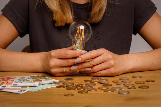 Worried woman holding a Classic electric light bulb in front of her  money scattered on the desk. Photo for Finance and energetic and high electricity bill prices concepts. 
 World economy crisis. 
