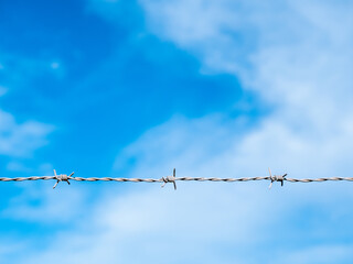 One strand of a barbed wire with blue sky and clouds in the background.