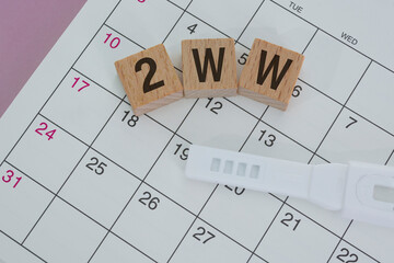 2WW word on wooden block with on calendar. Two Week Wait concept.