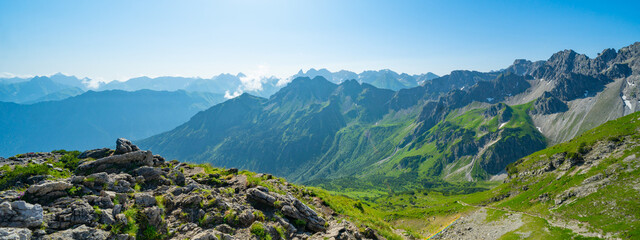 Fototapeta na wymiar Panoramic view from Nebelhorn in Oberstdorf Allgäu Bavaria Germany - Beautiful Alps with lush green meadow and blue sky - Mountains landscape background banner panorama.