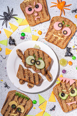 Funny halloween monster sandwiches. Set of various decorated monster sandwich and toasts, with cucumber, cheese and meat sausages, white table background with Halloween decorations