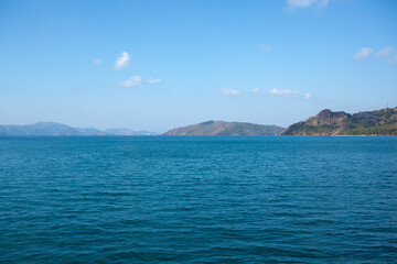 Fototapeta premium Summer seascape beautiful waves, blue sea water in sunny day. Sea bay with far hazed mountains on horizon. Fog in the mountains.