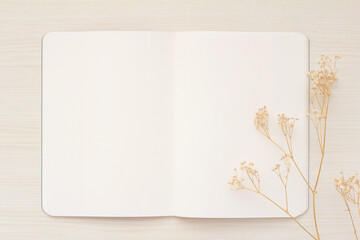 A white notebook with a white spread and hazelbaby’s breath on a light wood desk