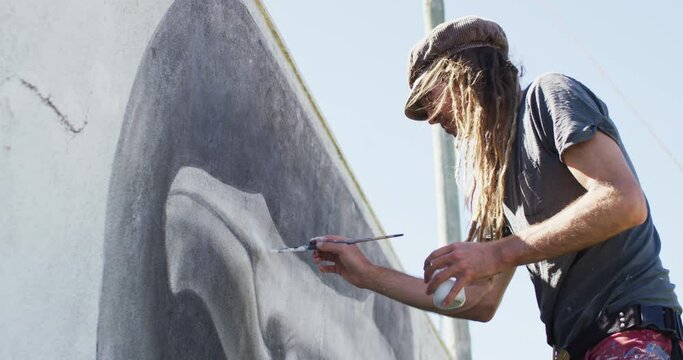 Video of caucasian male artist with dreadlocks painting whale mural on wall