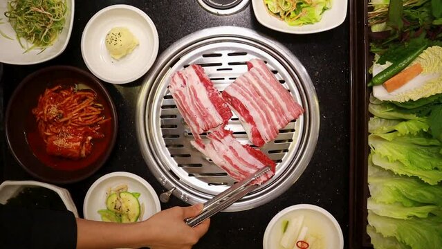 A scene where a female employee's hand puts the  Short Plate on a charcoal-grilled pan Used in a Korean Japanese Asian BBQ restaurant