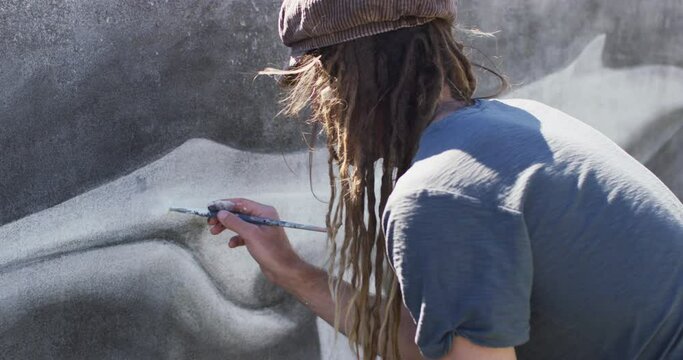 Video of caucasian male artist with dreadlocks painting whale mural on wall