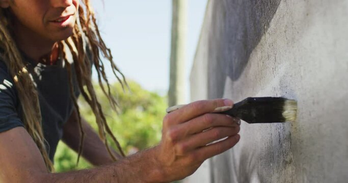 Video of caucasian male artist with dreadlocks using paintbrush painting whale mural on wall