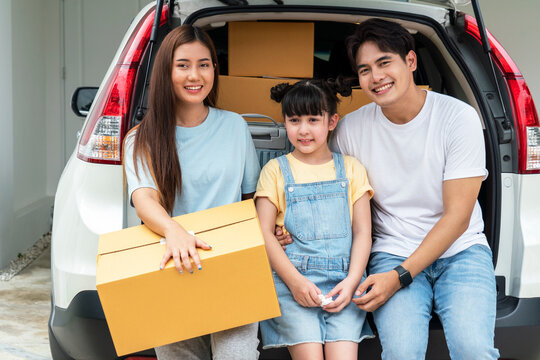 Asian Family, Parents And Daughters Sit In The Back Of A Car With Transport Boxes To Their New Home.