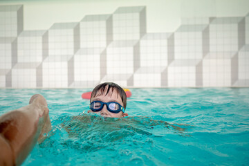 preschool boy playing in indoor pool with goggles on his eyes and smile on his face