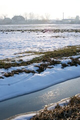 Winter view of field - meadow. Grass covered by snow. Frozen drainage ditch.