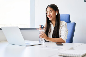 Young woman opening water bottle while working in office using laptop