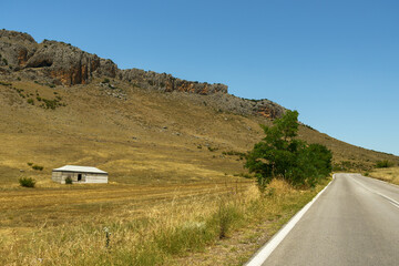 Obraz premium Asphalt road leading through rocky mountains and an abandoned house.
