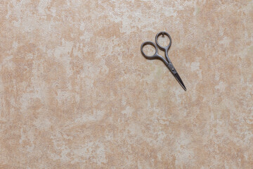 Manicure scissors hang on a small nail driven into the wall. Wall with wallpaper inside the house.