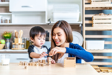 Young asian mother and little son enjoy to play wooden jigsaw puzzle together in area of kitchen of their house and they look happiness, childhood and motherhood concept