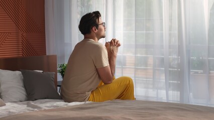 Young man sit on bed and pray looking up