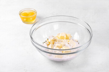 Cooking shortbread dough. Mixing flour, salt, dried herbs, butter and eggs in glass bowl on white table. Making crackers, tart, galette, pie or quiche