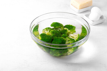 Blanching broccoli florets in cold water in glass bowl on white table. Cooking ingredient for salad, pie or side dish
