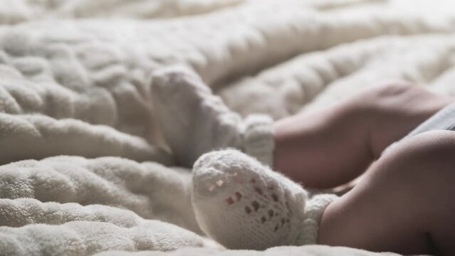 Infant baby feet on a bed. Newborn baby in warm socks laying on a bed.  Сute little baby feets lying on bed, white blanket. Еoddler moving gentle feet fingers. motherhood, baby care concept