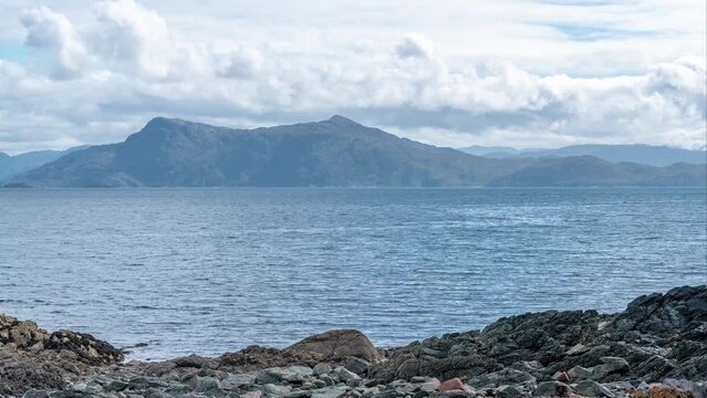 4K Timelapse of the Scottish sea from Isle of Skye  watching Scotland with clouds moving on top of a mountain in the distance on rocky beach  